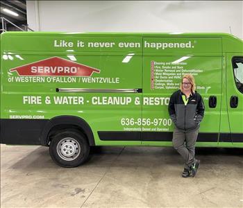 Female with blonde hair in SERVPRO uniform standing up against green van, smiling.