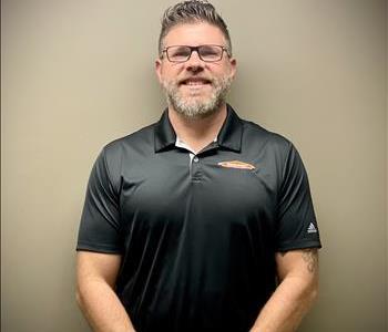 SERVPRO owner with brown hair and glasses in uniform smiling in front of a grey background.