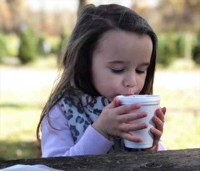 small child is sitting at a picnic table outside sipping hot chocolate from a Styrofoam cup.