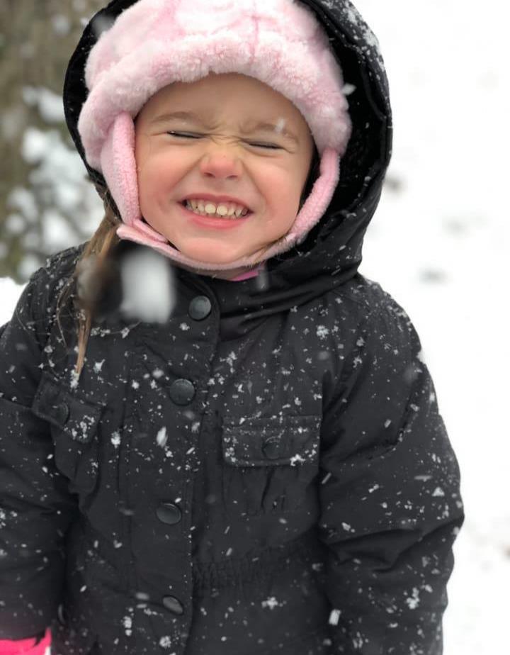 Jojo smiling big with a snow hat and coat on and snow all around her