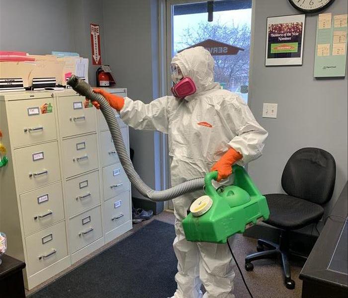Joanne, one of our owners, in full PPE holding a macromist mister and doing a preventative disinfecting of the office.